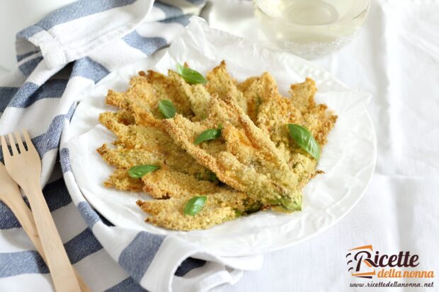 Fiori di zucca al forno croccanti con panatura ai cornflakes, con sopra foglie di basilico per decorazione, serviti su piatto bianco. Forchette di legno a lato.