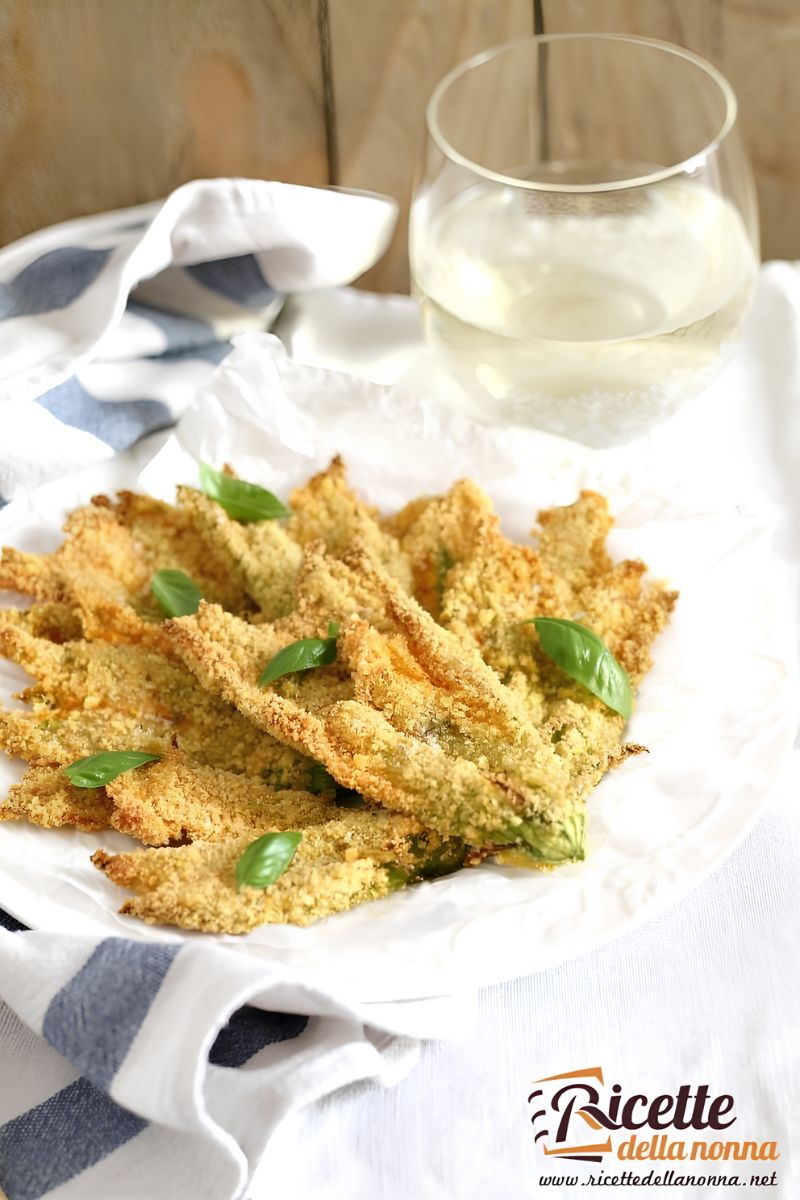 Fiori di zucca al forno croccanti con panatura ai cornflakes, con sopra foglie di basilico per decorazione, serviti su piatto bianco. Forchette di legno a lato. Primo piano.