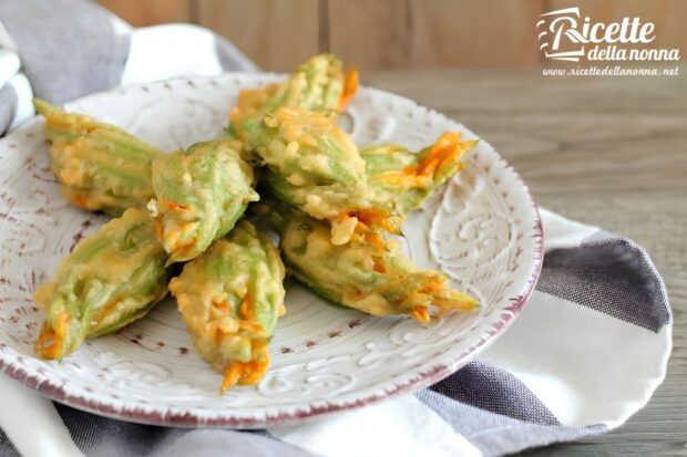 Fiori di zucca fritti in pastella croccante, disposti su un piatto decorato bianco con bordo marrone, su tovagliolo a righe bianche e grigie