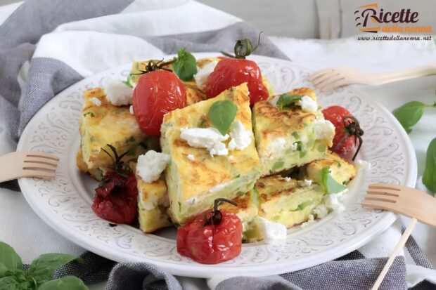 Frittata di zucchine tagliata a rombi con feta, pomodorini arrostiti e foglie di basilico, servita su un piatto bianco decorato
