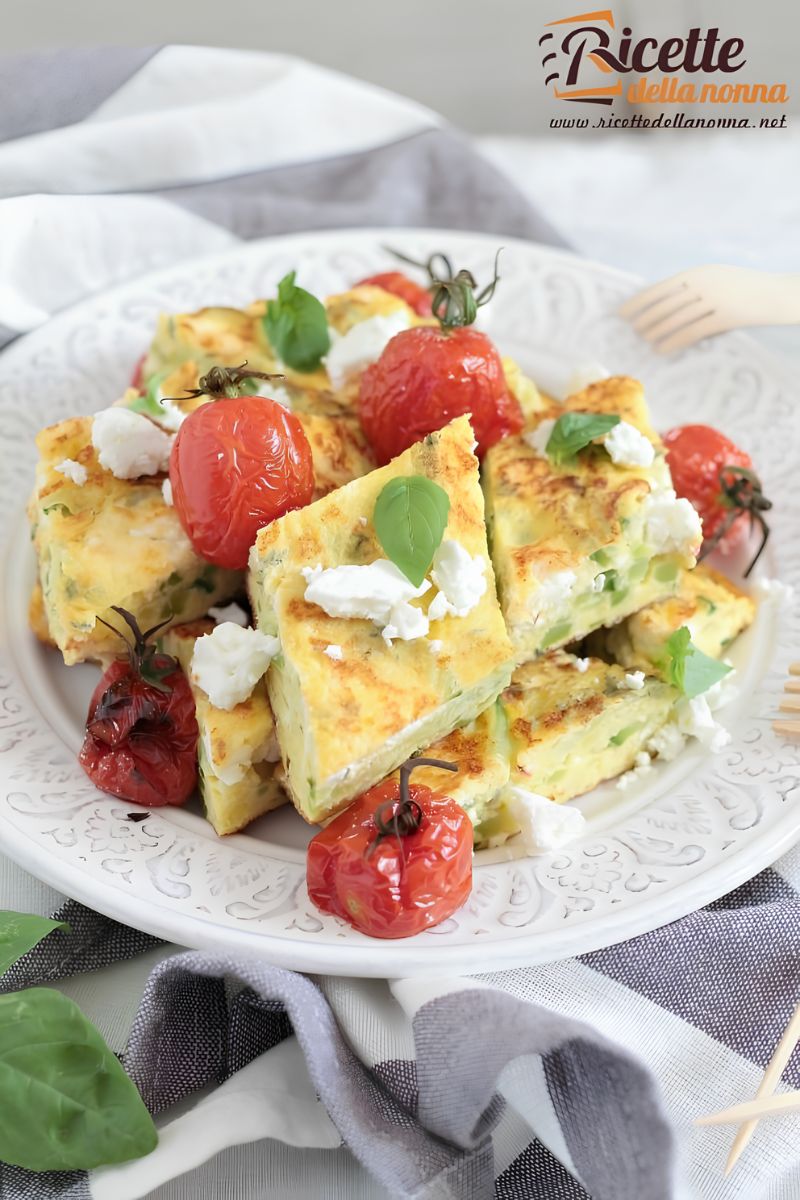 Frittata di zucchine tagliata a rombi con feta, pomodorini arrostiti e foglie di basilico, servita su un piatto bianco decorato