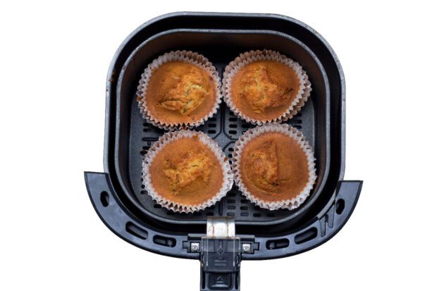 Quattro muffin al cacao in pirottini di carta bianca, cotti nel cestello di una friggitrice ad aria vista dall’alto.