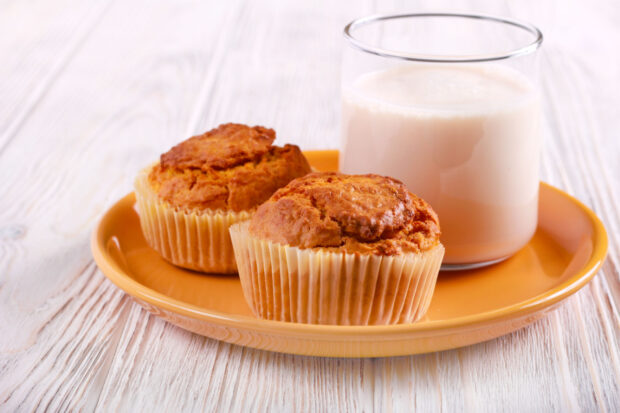 Piatto arancione con sopra due muffin ed un bicchiere di yogurt, su sfondo di legno
