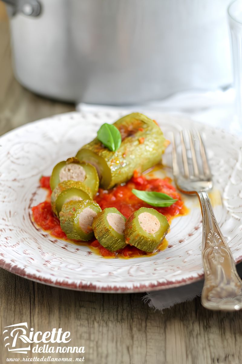 Zucchine ripiene tagliate a fette con ripieno di carne visibile, servite su piatto decorato con salsa di pomodoro e foglie di basilico. Primo piano