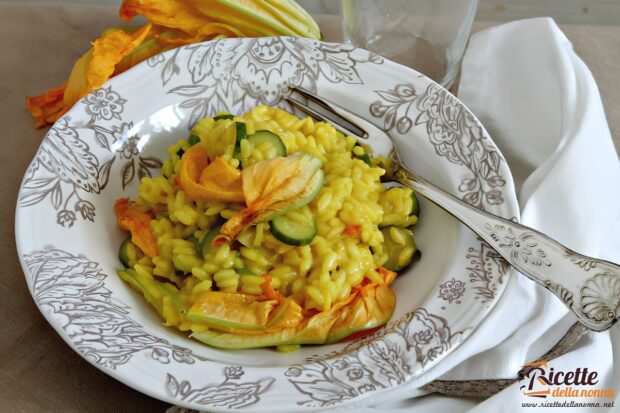 Piatto di risotto allo zafferano con zucchine e fiori di zucca, servito in un’elegante scodella decorata.