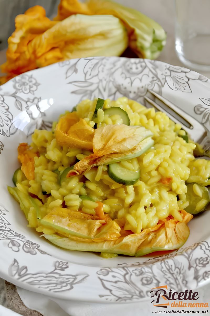 Risotto allo zafferano con zucchine e fiori di zucca, servito in piatto decorato. Primo piano.