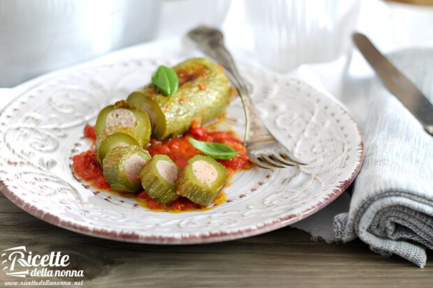 Zucchine ripiene tagliate a fette con ripieno di carne visibile, servite su piatto decorato con salsa di pomodoro e foglie di basilico