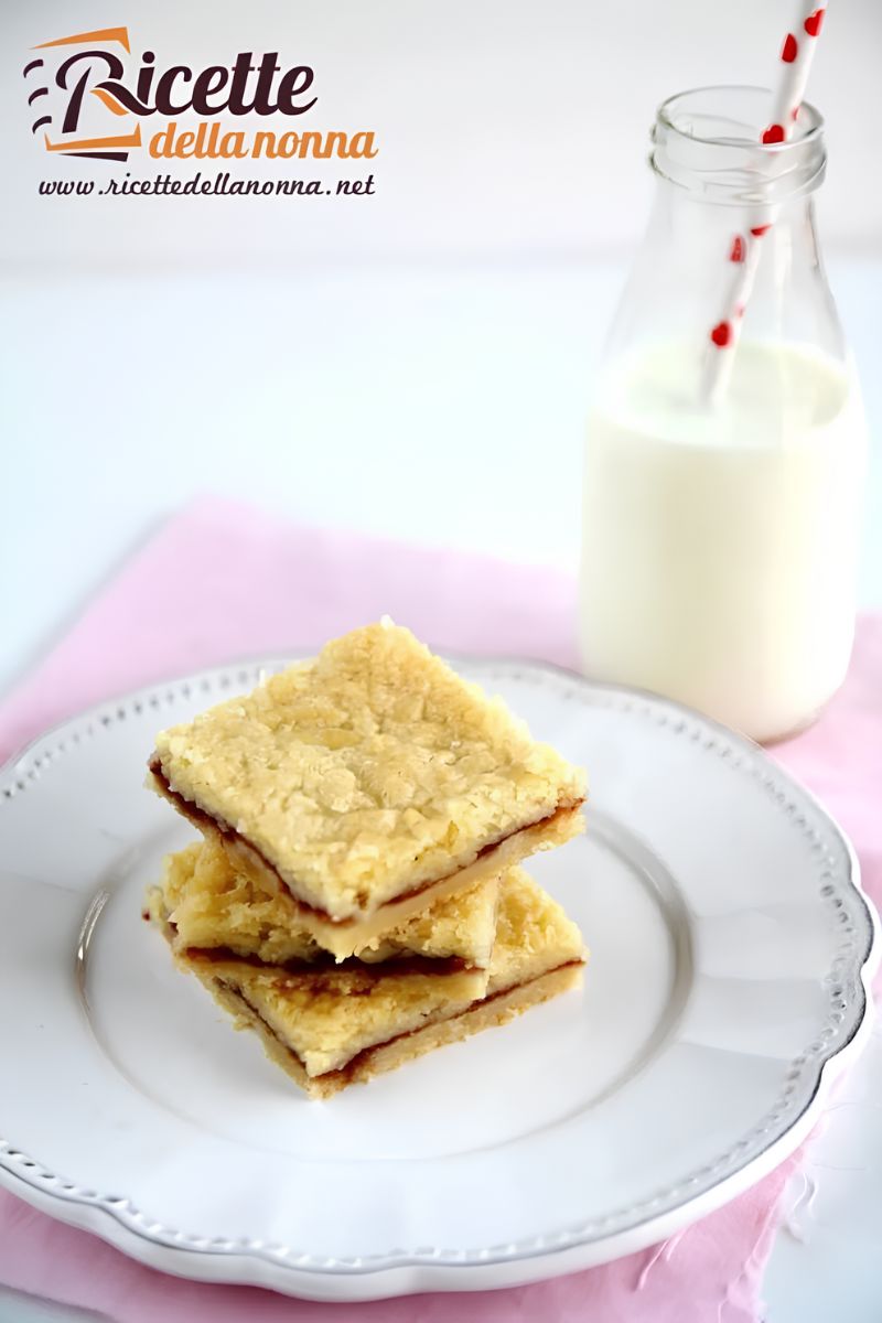 Barrette con marmellata di fragole impilate su un piatto, con vicino una bottiglia di latte in vetro con una cannuccia bianca e rossa