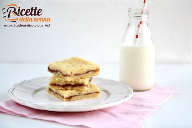 Barrette con marmellata di fragole impilate su un piatto, con vicino una bottiglia di latte in vetro con una cannuccia bianca e rossa