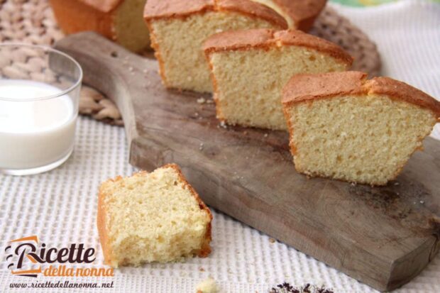 3 fette di ciambellone su un tagliere di legno ed una di lato, vicino ad un bicchiere di latte. Ciambellone rimanente sullo sfondo, in alto