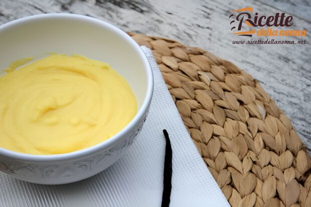 Ciotola bianca con crema pasticcera liscia e vellutata fatta con amido di mais, accanto a una bacca di vaniglia su tovaglietta intrecciata