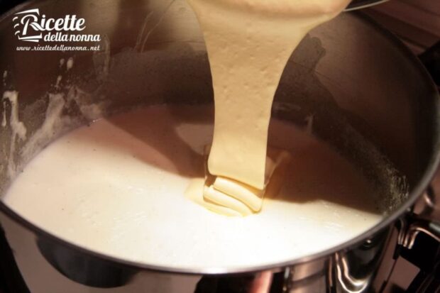 Impasto cremoso di uova, zucchero e amido di mais versato nel latte caldo in una casseruola durante la preparazione della crema pasticcera