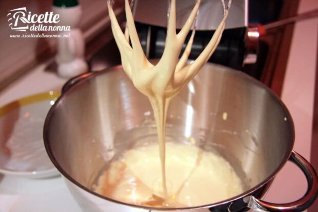 Fruste elettriche sollevano un composto cremoso di uova e zucchero montati in una ciotola di acciaio durante la preparazione della crema pasticcera con amido di mais
