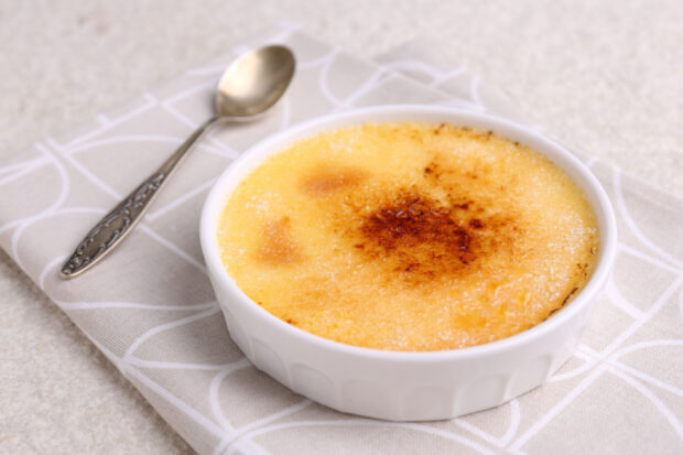 Creme brulee salata servita in una cocotte con accanto un piatto, su una tovaglia grigia.