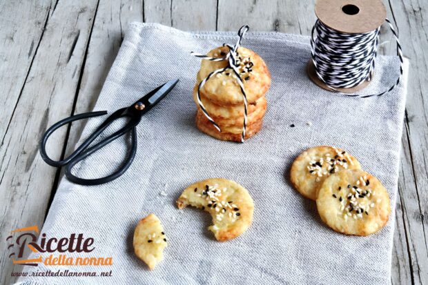 Crocchette di patate tonde al sesamo e semi di papavero su un canovaccio grigio, con forbici e spago decorativo. Alcune sono impilate e legate con lo spago bianco e nero