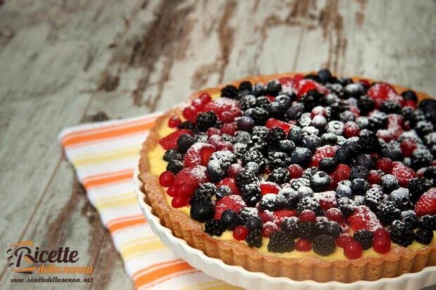 Crostata ai frutti di bosco con crema pasticcera, intera, su un piatto. Sfondo di legno