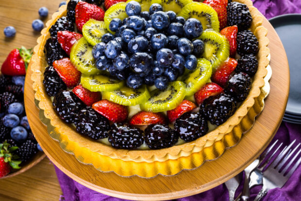 Crostata di frutta e cioccolato con base di pasta frolla, decorata con fragole, kiwi, more e mirtilli disposte a cerchio