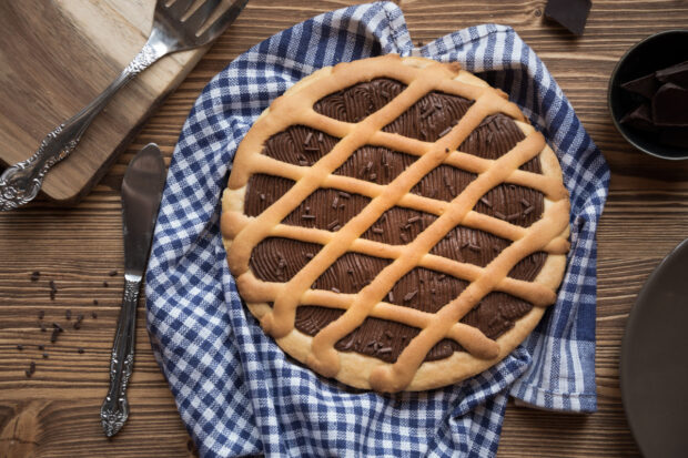 Crostata pere e cioccolato, visibilmente morbida, su una tovaglia a quadri bianca e blu, sfondo di legno