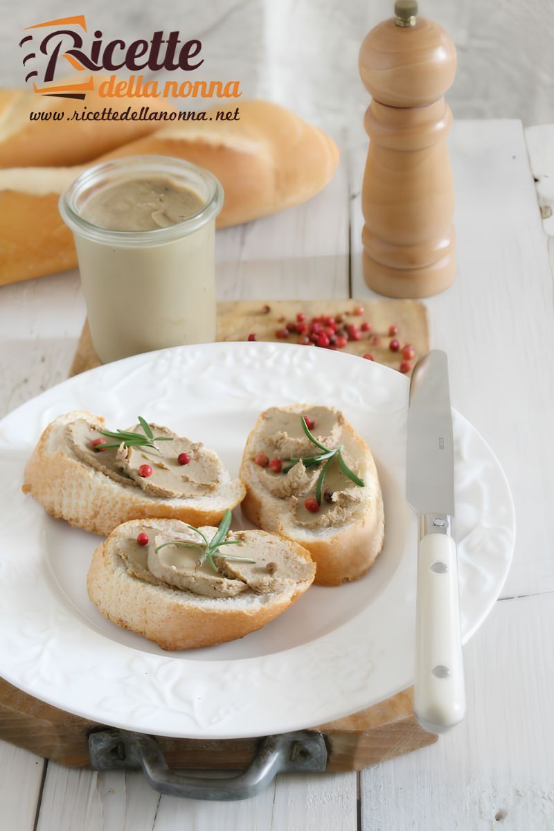Tre crostini neri toscani con paté di fegato toscano serviti su un piatto. Sfondo di legno, sopra due pagnotte, un macinapepe ed un bicchiere con una bevanda