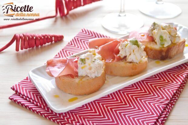Tre crostini yogurt zucchine e bresaola su un piatto bianco, sopra una tovaglia rossa