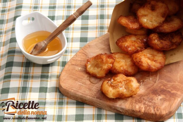 Frittelle di patate dolci, fritte, su un tagliere di legno in un cartoccio di carta. Vaschetta di miele vicino, su una tovaglia