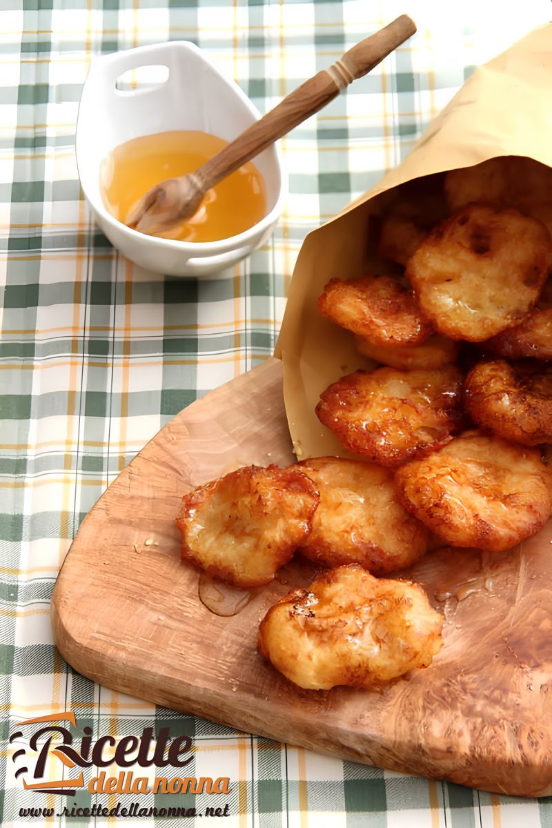 Frittelle di patate dolci fritte, su un tagliere di legno in un cartoccio di carta. Vaschetta di miele vicino, su una tovaglia