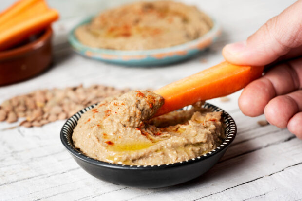 Ciotola di hummus di lenticchie guarnito con olio extravergine e paprika, servito con bastoncini di carote