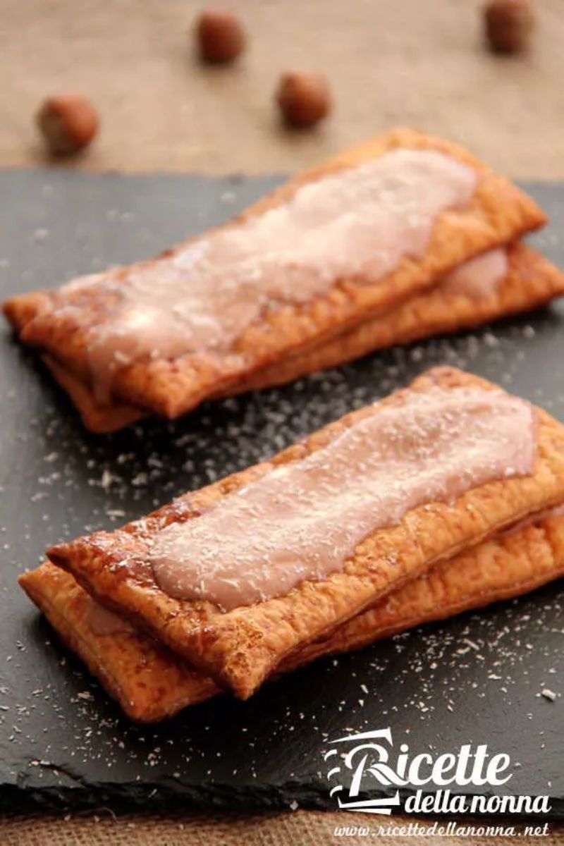 Dolce millefoglie fatto con pasta sfoglia pronta, farcito da una crema di yogurt e Nutella tra gli strati e coperto da cocco rapè, servito su un vassoio nero. Primo piano