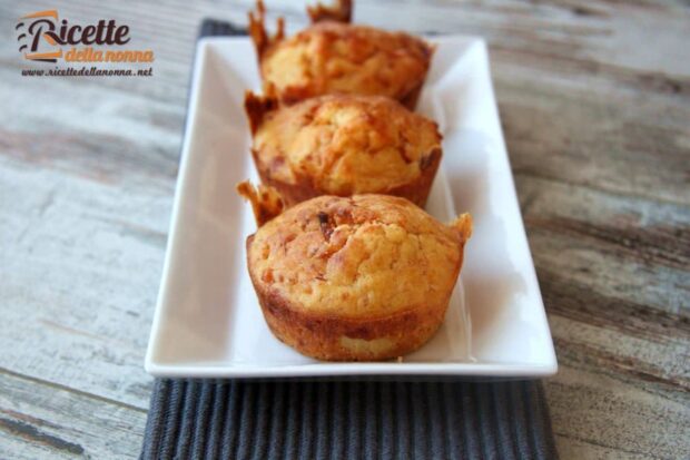 Tre muffin con prosciutto e formaggio in una piccola terrina bianca su un piccolo ripiano nero. Sfondo di marmo