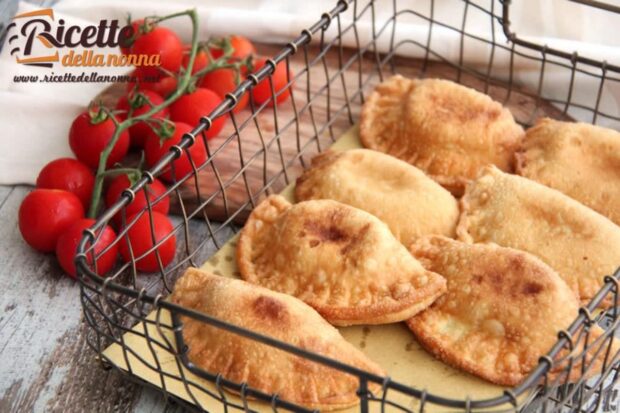 Panzerotti ripieni messi in un cestino decorativo con accanto dei pomodori