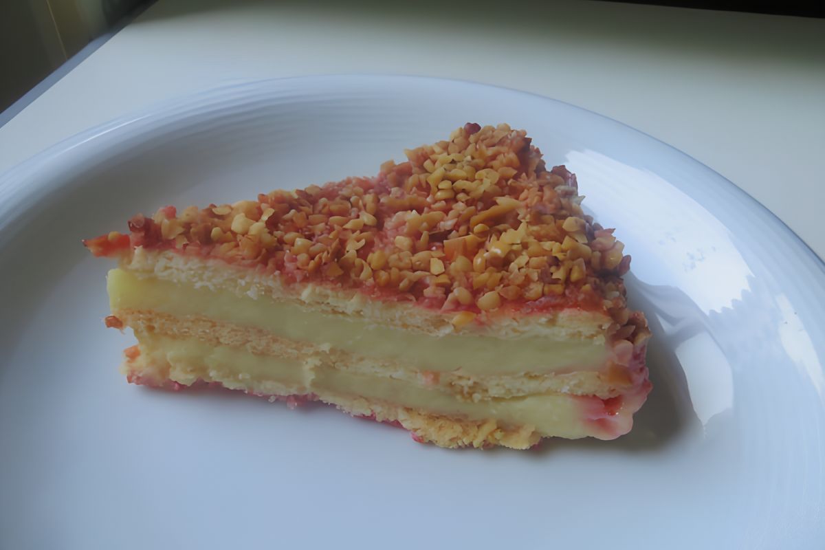 Fetta di torta Millefrolle con crema, fragole e granella di nocciole, su un piatto, sfondo bianco