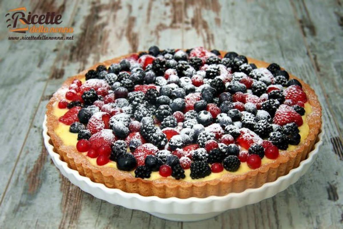 Crostata ai frutti di bosco con crema pasticcera, intera, su un piatto. Sfondo di legno
