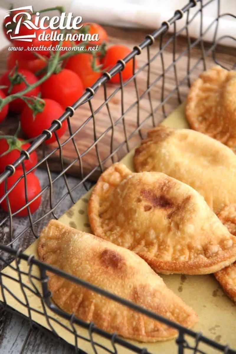 Panzerotti ripieni messi in un cestino decorativo con accanto dei pomodori. Primo piano