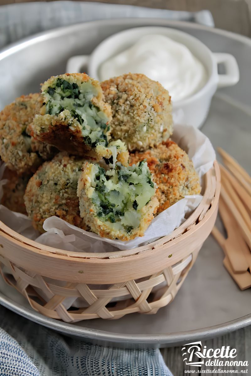 Polpette di patate, spinaci e provola servite in un cestino di vimini con vicino della panna acida e degli stecchini