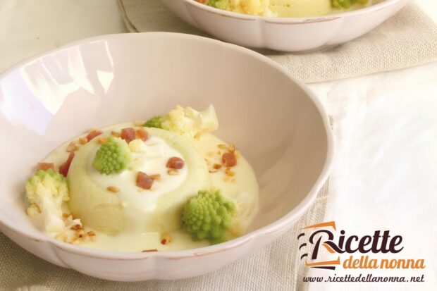 Sformato di broccolo romanesco con fonduta di formaggio brie, decorato da cimette di broccolo, cubetti di speck e granella di nocciole, servito in una ciotola chiara