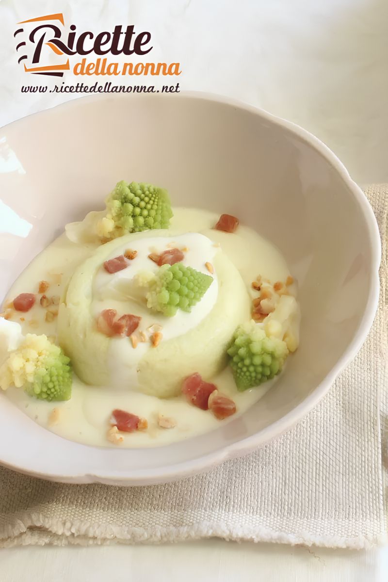 Sformato di broccolo romanesco con fonduta di formaggio brie, decorato da cimette di broccolo, cubetti di speck e granella di nocciole, servito in una ciotola chiara