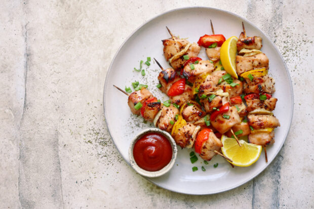 Piatto con 4 spiedini di coniglio, una fetta di limone e una ciotolina di ketchup. Sfondo di marmo