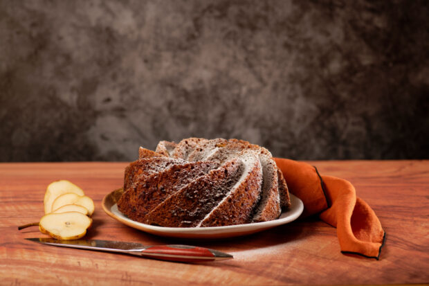 Torta fatta con mandorle e pere, fumante su un tavolo di legno con accanto due pere ed un coltello