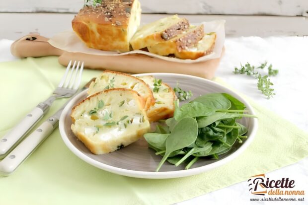 Fette di tortino di zucchine con pezzi di formaggio, con vicino spinaci a decorazione, in un piatto; tortino di zucchine intero sullo sfondo