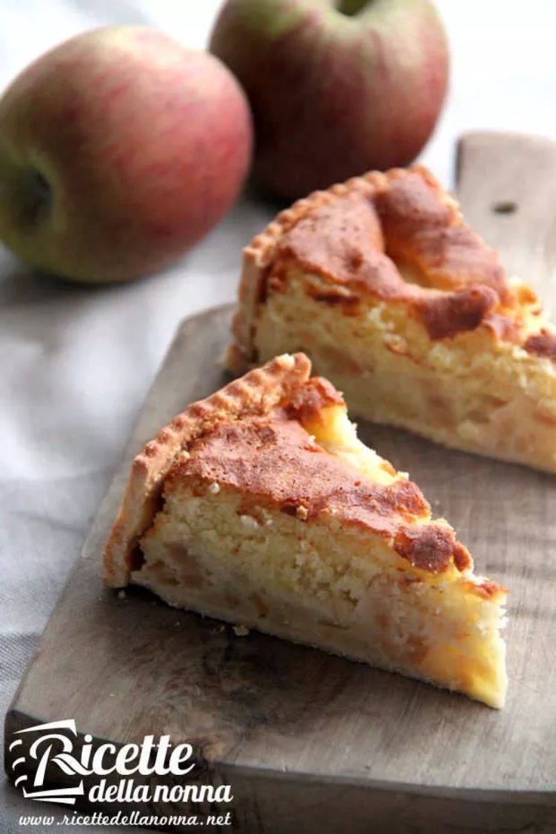Primo piano di due fette di torta di mele meringata su tagliere di legno. Due mele verdi sullo sfondo