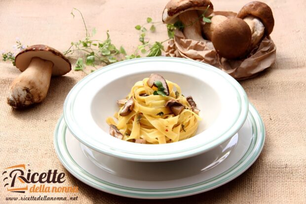 Tagliatelle ai funghi porcini su un piatto bianco, con accanto dei funghi porcini